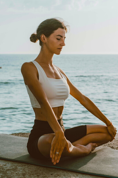 An adult woman practices meditation on a yoga mat by the sea, embracing the calmness and stillness of the outdoors