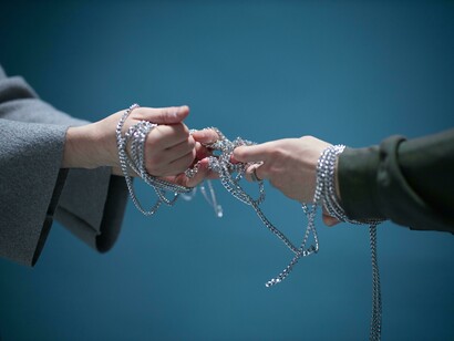 Hands untangling a silver chain representing tension amongst political thoughts 
