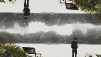 A man standing in front of a park bench, creating an optical illusion that distorts perception