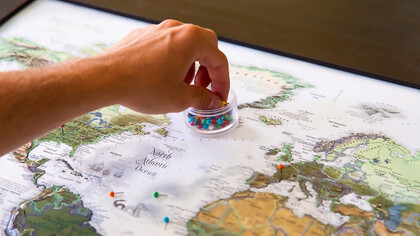 A person placing push pins into a world map, symbolizing the power of naming, cartography, and the marking of geopolitical boundaries