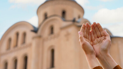 A woman with open hands stands beside a religious building during a spiritual visit