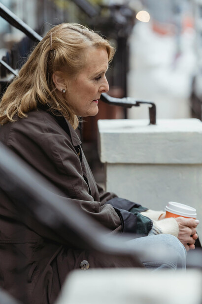 A solitary, melancholic woman on an urban bench with a takeaway coffee, quietly lost in thought in the midst of the city