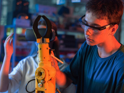 A person wearing protective glasses interacts with a robot in a high-tech robotics laboratory
