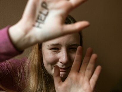 A terrified woman shows the word “Help” written on her palm, representing the hidden reality of emotional abuse