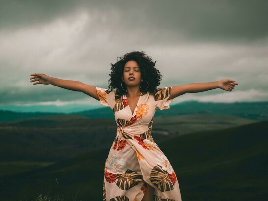 A woman in a white and red floral dress standing on a green grass field, representing freedom, self-acceptance, and openness