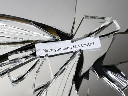 A shattered mirror encircling a note that reads “Have you seen the truth?”, representing the fragmentation of reality in modern media