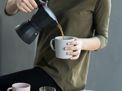 Woman wearing green blouse brews filter coffee and pours it into a cup