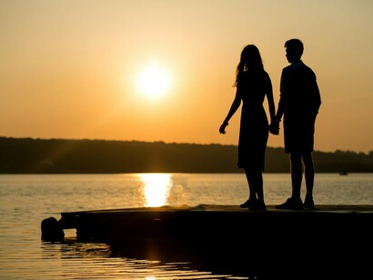 A couple standing by the riverbank at dusk, reflecting the fleeting calm before their world changed forever