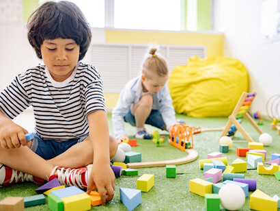 Crianças brincam em atividade lúdica no chão de grama de uma sala escolar