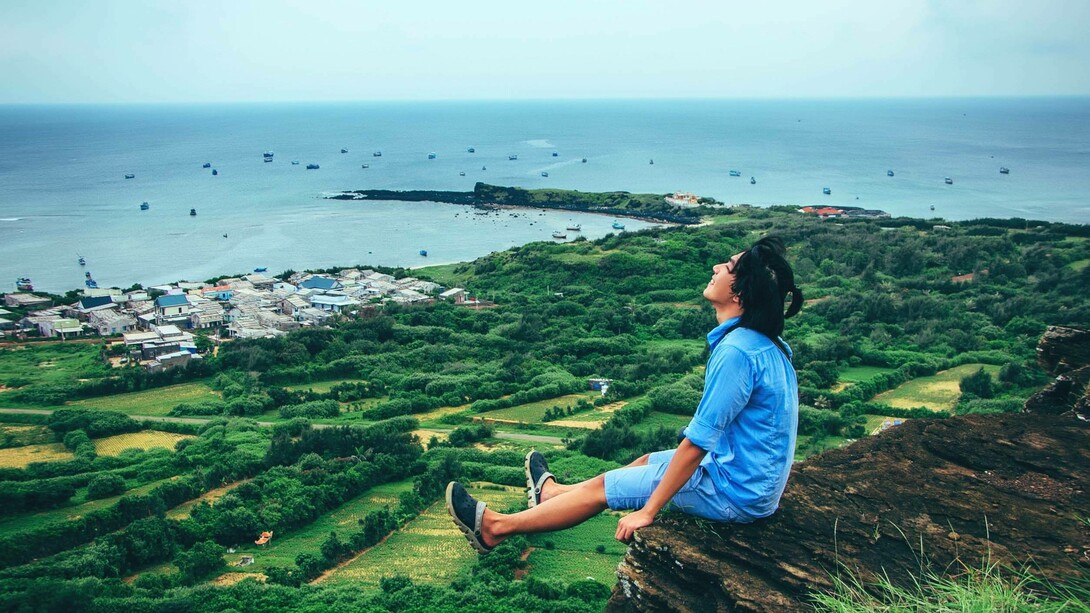 A man dangling his legs over a cliff smiling and taking in the breathtaking scenery in Phú Quốc, Vietnam