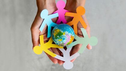 A top-view image of interconnected origami people forming a chain around the globe, symbolizing unity, peace, and vibrant diversity with an array of colors