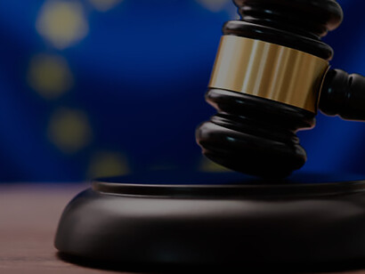 A wooden gavel rests on a table alongside the flag of the European Union