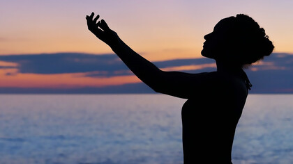 Silhouette of a woman stretching her hands to the sky, believing and wishing