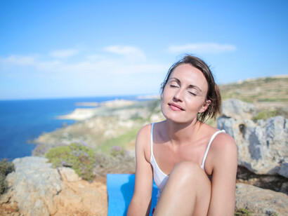 A woman finishes her yoga routine with meditation near the sea