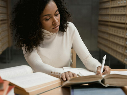 A woman researching in a library at a table covered with books