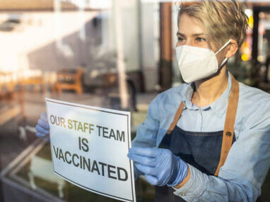 A restaurant owner holds a sign announcing that all employees are vaccinated against COVID-19 as the restaurant prepares to reopen after the pandemic