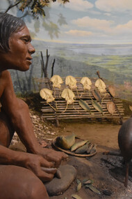 Life in the Jōmon period as recreated at the Municipal Museum of Archaeology in Ichikawa: a prehistoric woman sits before a fire where fish are being grilled on skewers, and, behind her, a heap of discarded clamshells (shell midden) and a wooden rack on which whole squids are being dried