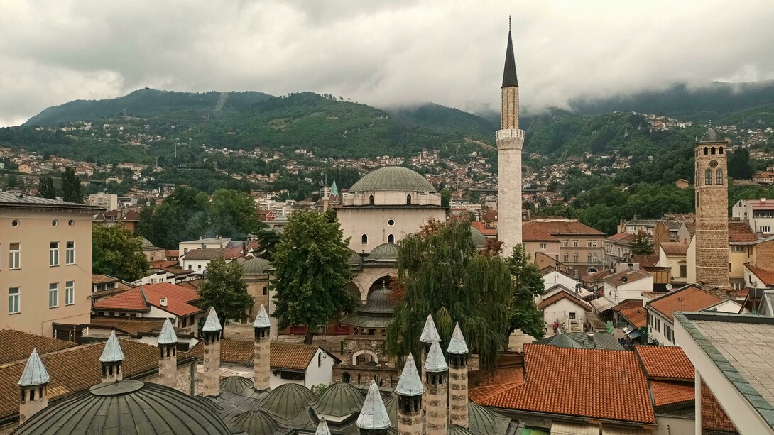 Vista Panorâmica Da Arquitetura Histórica De Sarajevo. Ao chegar a Sarajevo, fui imediatamente arrebatada pela paisagem que circunda a cidade e pela arquitetura variada, refletindo séculos de dominação otomana, austro-húngara e, mais recentemente, os traços deixados pela antiga Iugoslávia. Caminhar por suas ruas é como folhear as páginas de um livro de história vivo