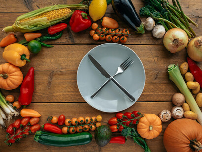 A plate with a knife and a fork on top, between assorted vegetables on a table