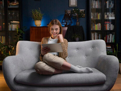 At home on a cozy couch, a woman scrolls through her phone, surrounded by the subtle power of digital media and online content