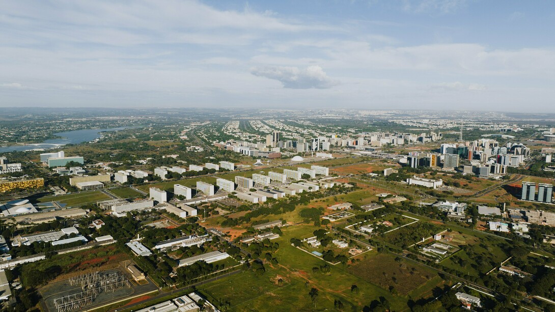 Do alto, Brasília revela o contraste entre o desenho urbano planejado e a expansão que se estende para além de seus limites. Ao fundo, as cidades-satélite aparecem distantes do núcleo original, evidenciando como o crescimento efetivo pode assumir trajetórias diferentes daquelas previstas pelo planejamento