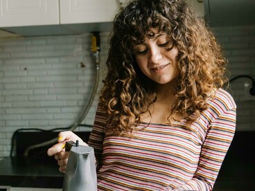 A calm kitchen scene shows a woman making coffee at home in gentle light