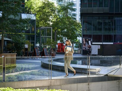 A woman using her phone in a well-designed civic plaza, reflecting the role of open, visible environments in crime prevention 