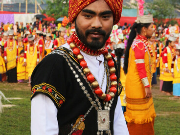 A Khasi man in traditional attire alongside performers in vibrant traditional costumes during a cultural parade in Meghalaya, India