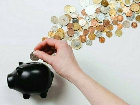 A hand placing a coin into a piggy bank, representing the steady growth of collectible value over time