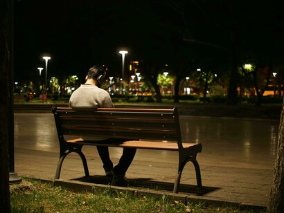 A solitary man sits on a bench at night in an urban park, capturing the feeling of isolation, urban loneliness, and a disconnected society