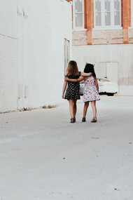 Two girls walk down the street, embracing each other in a warm hug, sharing a moment of kindness and connection