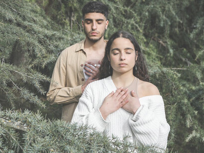 Amidst the verdant greenery, a couple stands with their hands gently placed over their chests