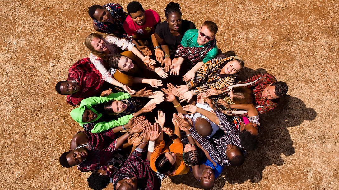 People from diverse backgrounds gather in a circle in Masimba, Tanzania, expressing solidarity and community through a shared gesture of unity