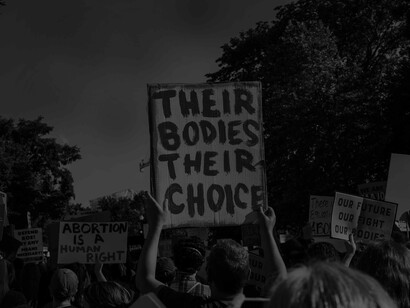 A sign reading 'their bodies, their choice' is held up by someone white and male who is supporting the choices for women and evoking that he treats all as his equal