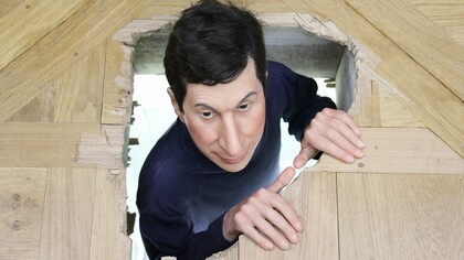 Esta escultura em tamanho real é um autorretrato. O artista olha para cima através de um buraco no chão. O cômodo abaixo parece ser um depósito, mas na verdade é o vestiário dos funcionários. Aqui Cattelan faz um jogo convincente com a realidade e a imitação, minando as expectativas do espectador