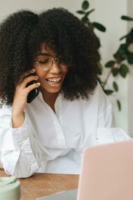 A Gen Z woman sits in front of her laptop and tablet, multitasking between work and digital tasks, and speaking on the phone