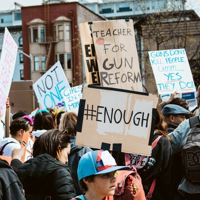 A diverse crowd of protestors holding bold, handmade signs demands urgent action against the ongoing epidemic of gun violence in America