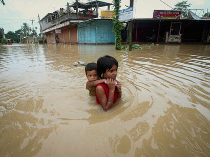 Una niña carga a su hermano mientras atraviesa un camino inundado después de fuertes lluvias en las afueras de Agartala, India, el 18 de junio de 2022
