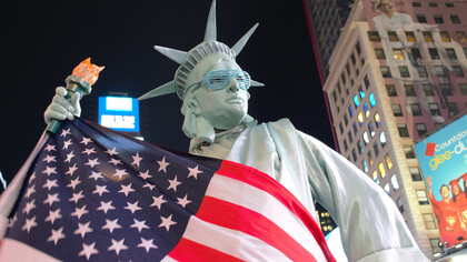 The Statue of Liberty draped in the American flag, wearing sunglasses