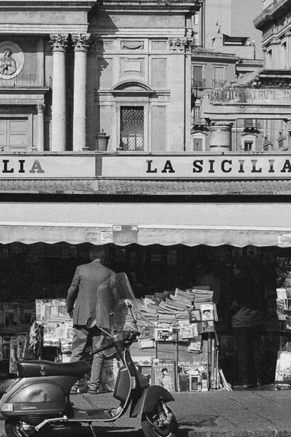 A scooter parked in front of a small kiosk in Sicily, Italy, a quiet scene reflecting everyday life amid lingering inequality and corruption