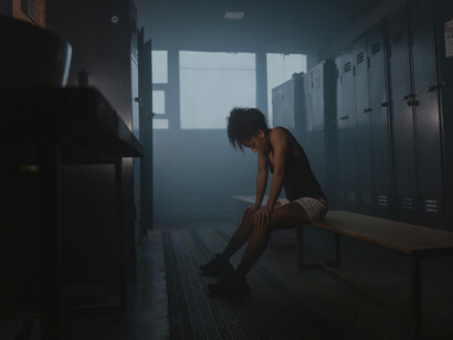 A woman alone in a dimly lit locker room, the empty space around her highlighting a sense of isolation and focus