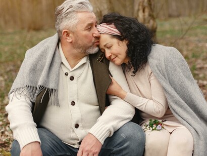 A couple sat together in the woods with a blanket over their shoulders