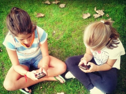 Dos chicas sentadas en el parque hablando con sus teléfonos