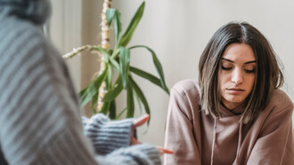 Ragazza siede pensierosa dinanzi una persona che cerca di comunicare con lei
