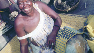 Ill. 1. Tonguoy Diarra pausing during the painting of the sleeve of a man’s tunic. The sleeve bearing the “Piece of a gourd” (Filen koloni) pattern is stretched across an empty calabash. Dyers always use the calabash as a support because it enables them to hold the metal spatula vertical to the cloth and to work on very small areas without staining other sections of the design. Kolokani.  
Photocredit Sarah C. Brett–Smith  

