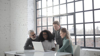 Sports managers collaborate around a computer, strategizing the future of sport management in an ever-evolving industry