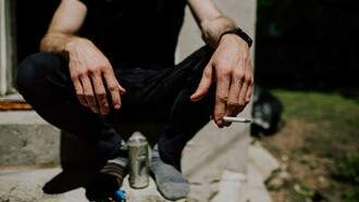 A person sitting on a step with a can and a cigarette 