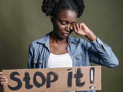 A woman in a blue denim jacket holds a brown cardboard sign, expressing feelings of being overlooked and misunderstood