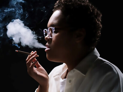 Captured in close-up, a woman donning white sleeves and stylish eyeglasses indulges in a compelling smoking moment