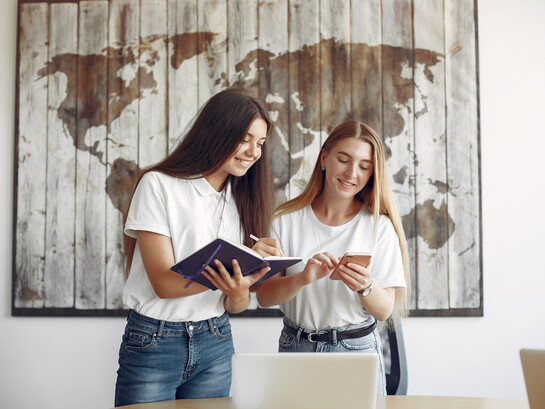Two exchange language students in white T-shirts working in an office in front of a world map